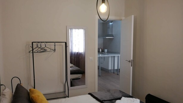 Habitación de hotel con cama, lámpara colgante, perchero y vista al área de la cocina.