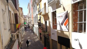 Una calle urbana estrecha flanqueada por edificios, algunos con balcones y letreros de negocios.