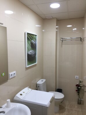 A bathroom with a toilet, bidet, and sink. There is a towel rack and a framed picture on the wall.