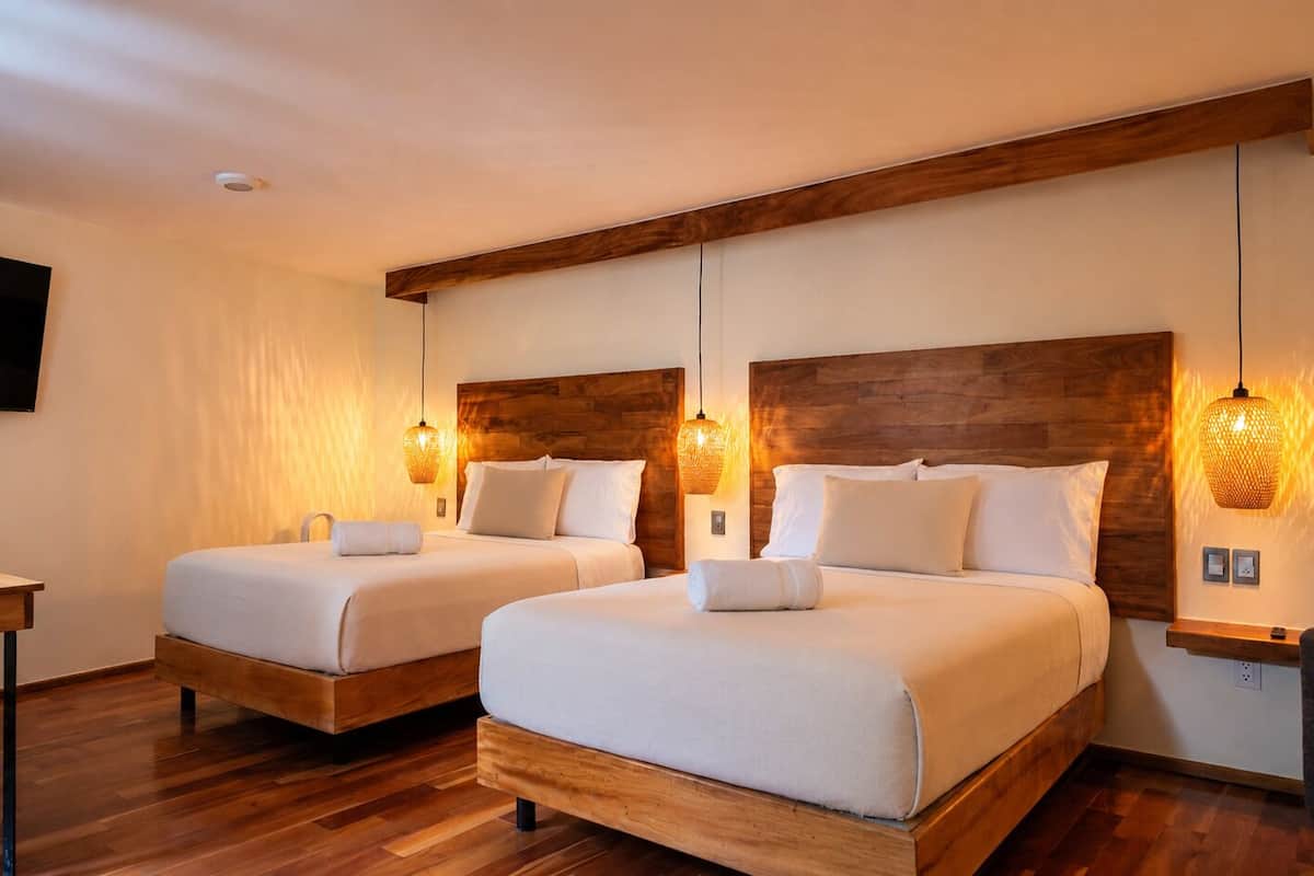 A hotel room with two beds, wooden headboards, and wall-mounted lamps.