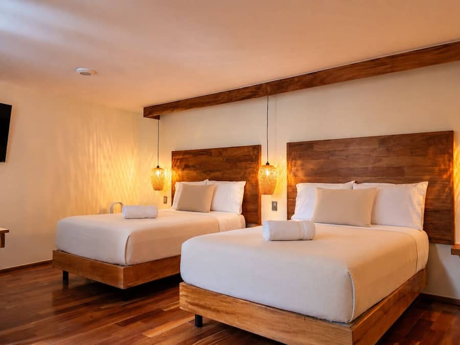 Habitación de hotel con dos camas, cabeceros de madera y lámparas fijadas a la pared.