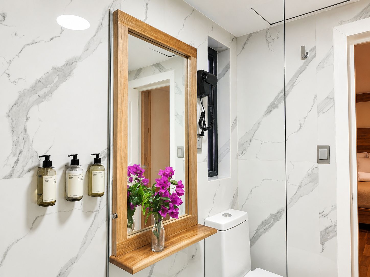A bathroom with a marble wall, a wooden vanity, a mirror, and a toilet.