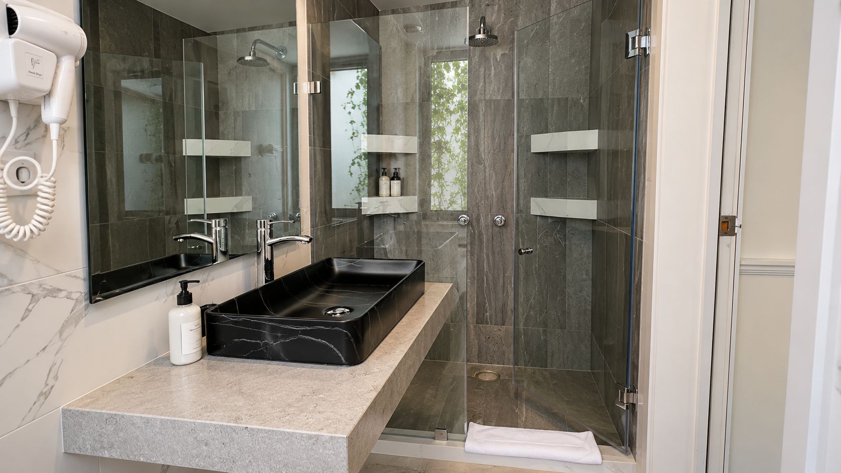 A modern bathroom with a large mirror, a black sink, and a glass-enclosed shower.