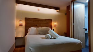 A neatly made bed with a wooden headboard, two bedside lamps, and a rolled towel on the bed.