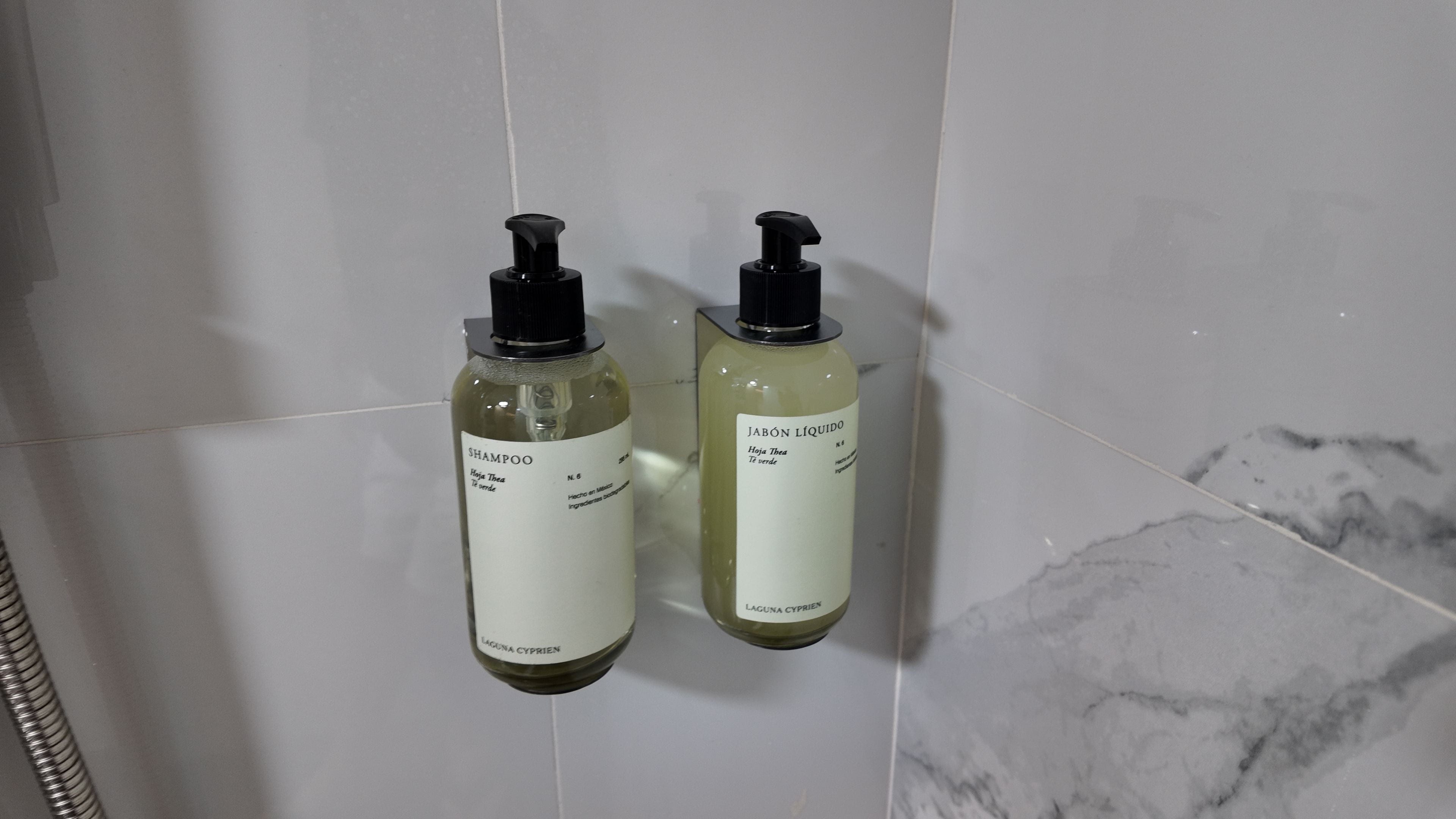 Two bottles of shampoo on a tiled wall.