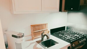 A kitchen with a coffee maker, sink, stove, and wooden rack. - Walk to Beach! - Cozy SC Studio (San Clemente)