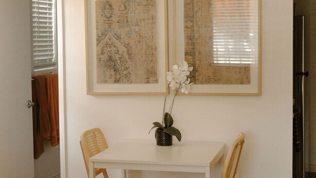 A dining area with a white table, four wicker chairs, two framed artworks, and a potted orchid. - Walk to Beach! - Cozy SC Studio (San Clemente)