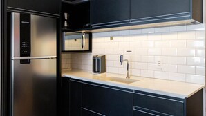 Una cocina moderna con un refrigerador de acero inoxidable, microondas integrado, cafetera y un lavamanos con grifo.
