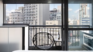 Una habitación moderna con un ventanal grande, una silla negra y una pequeña mesa con una botella.