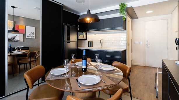 A modern dining area with a round table set for four, a wine bottle, and a hanging pendant light. - Condomínio Setin Downtown Genebra (São Paulo)
