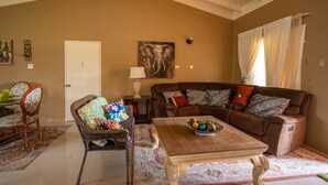 A living room with a brown sofa, a coffee table, a wicker chair, and a dining table with chairs. - Trove Manor (St. Ann's Bay)