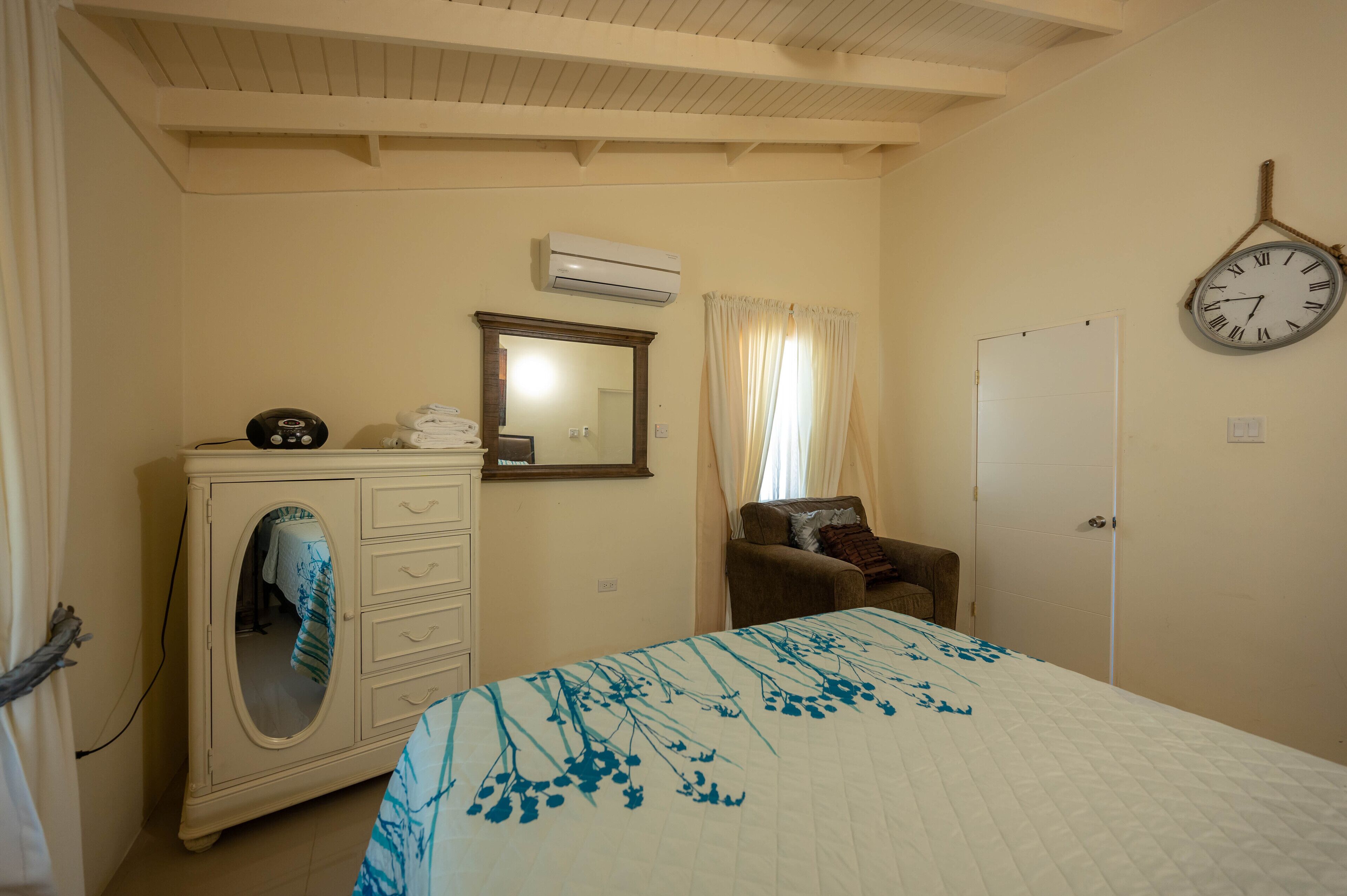 Un dormitorio con cama, cómoda, espejo, aire acondicionado, reloj y puerta.