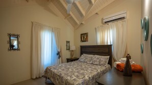 A bedroom with a bed, a nightstand, an air conditioning unit, and a wall-mounted mirror. - Trove Manor (St. Ann's Bay)