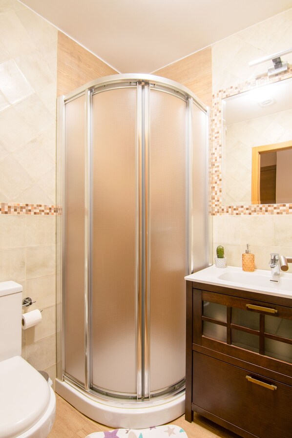 A bathroom with a glass-enclosed shower, a toilet, a sink with a mirror, and a cabinet with drawers.
