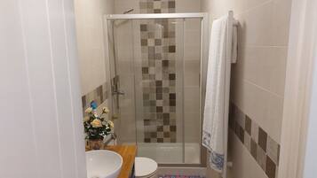 Un baño con ducha envuelta en vidrio, un lavabo blanco, un inodoro y un felpudo estampado.