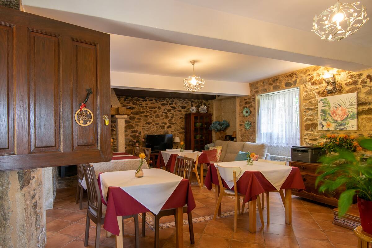 A dining area with wooden tables and chairs, stone walls, and a stone fireplace.