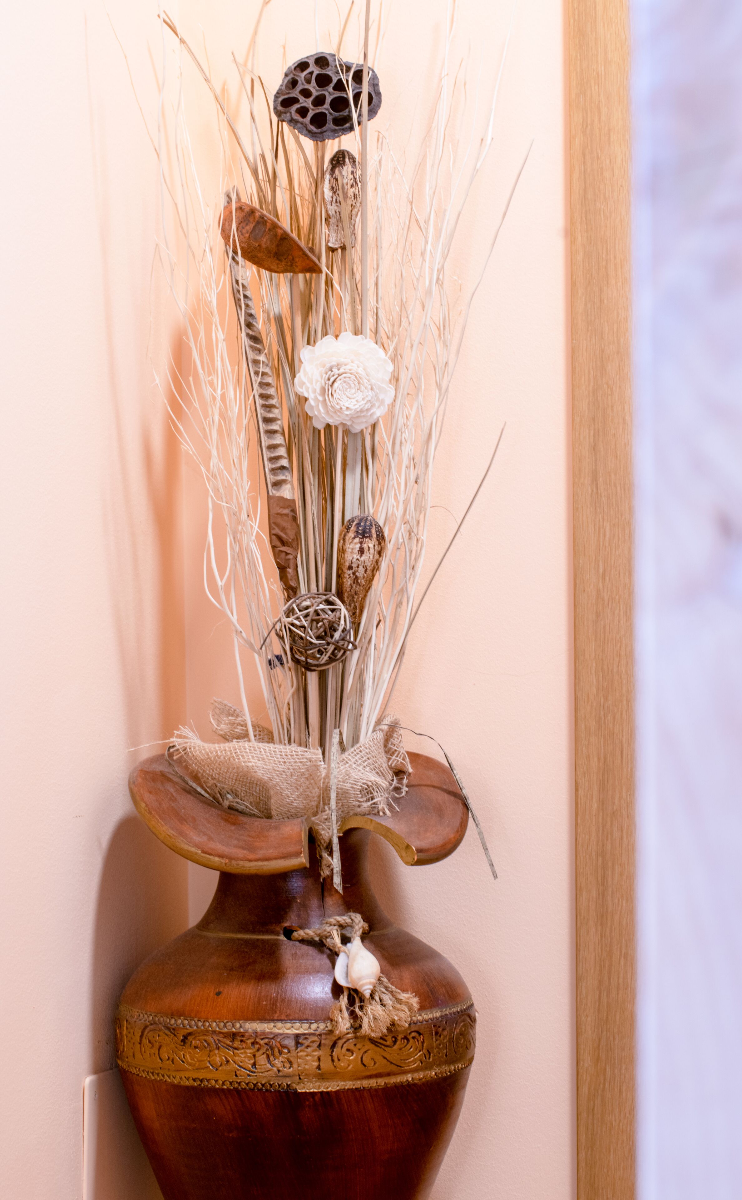 Un jarrón decorativo con un diseño rústico, que incluye elementos naturales como ramitas, flores secas y una pequeña figura de un búho.