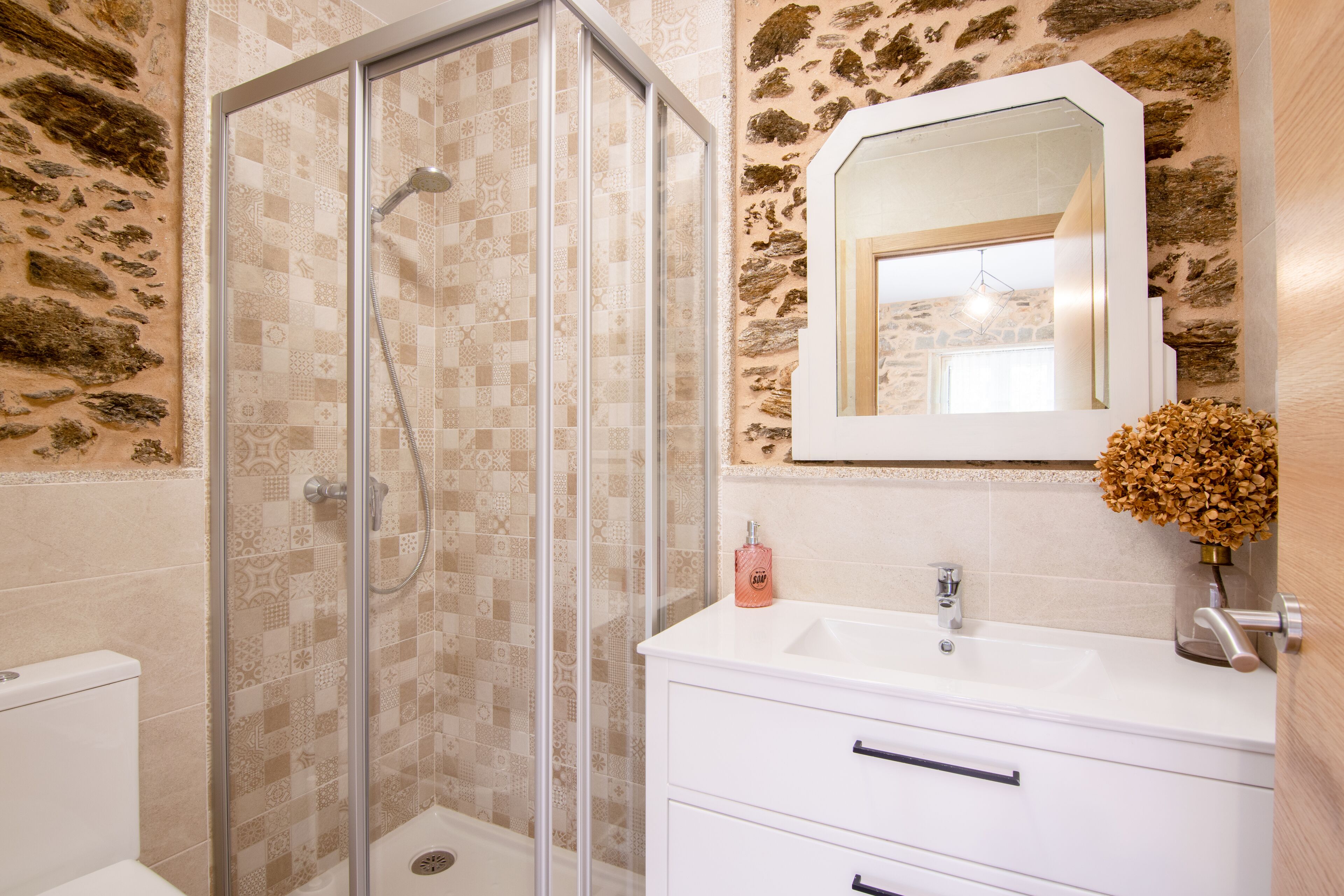 A bathroom with a glass-enclosed shower, a white sink, and a mirror above it.