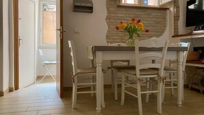 Un coin repas avec une table dressée pour quatre personnes, entourée de chaises blanches. Un vase rempli de fleurs est posé sur la table, et une inscription sur le mur indique : « Chez soi, on est bien. »