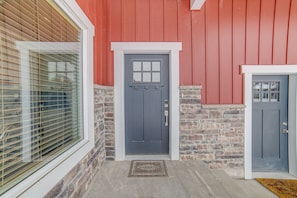 A house with a red exterior, a gray front door, and a window with blinds.