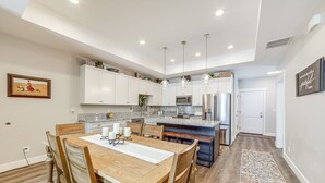 A modern kitchen with white cabinets, a wooden dining table, and pendant lighting.