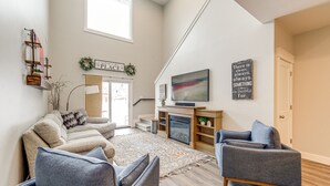 A spacious living room with a fireplace, a large flat-screen TV, and a cozy seating area with two armchairs and a sofa.