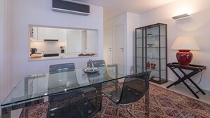 Ein moderner Essbereich mit einem Glastisch, Stühlen, einer Küche im Hintergrund, einem Glaskasten und einer roten Lampe.