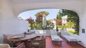 Eine sonnendurchflutete Terrasse mit einem runden Tisch, Korbstühlen und Liegestühlen.