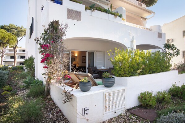 A modern white building with a balcony, potted plants, and a small garden area.
