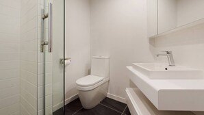 A modern bathroom with a glass shower enclosure, a white toilet, and a white sink with a mirror above it.