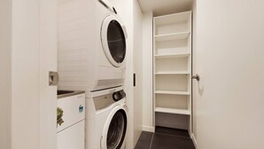 A laundry room with two stacked washing machines and a shelving unit.