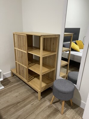 A room with a wooden wardrobe, a grey ottoman, and a bed with yellow pillows.