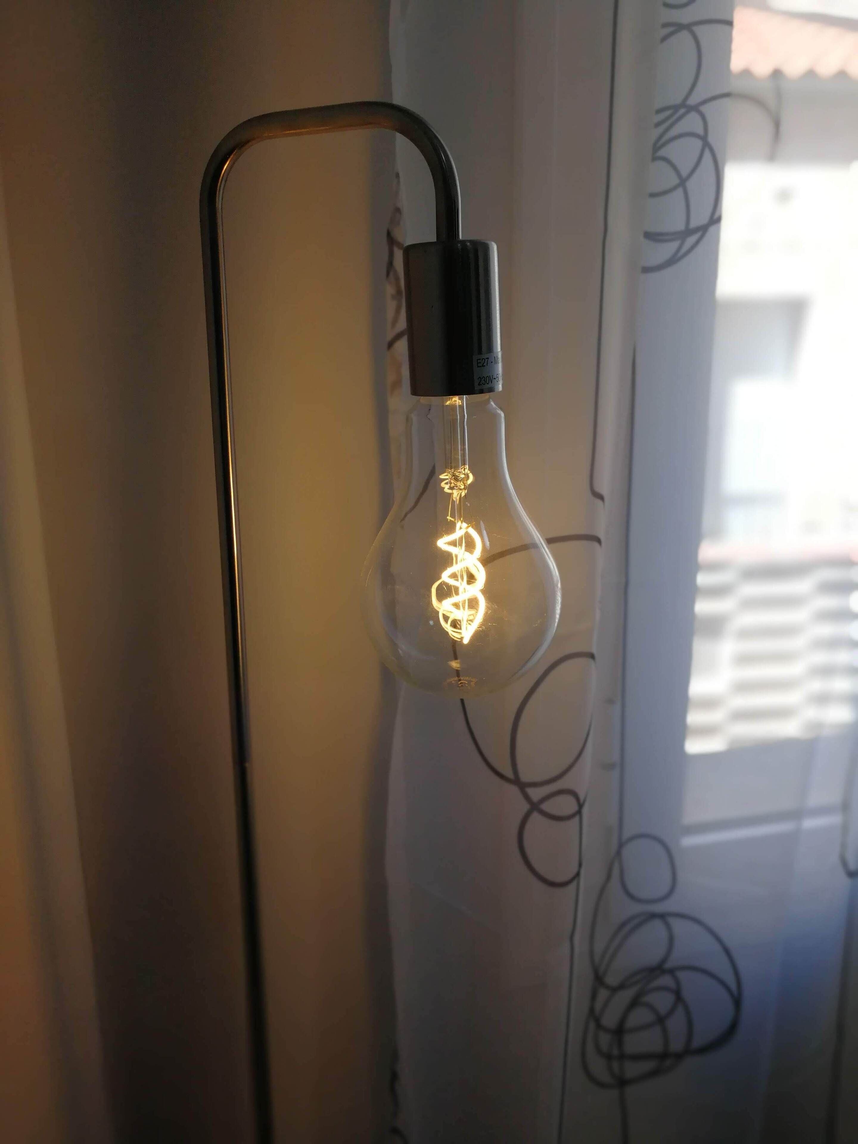 A light bulb with a black base and a clear glass enclosure, hanging from a black metal fixture.