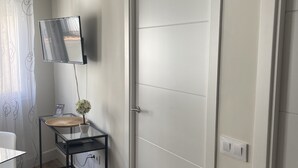Une pièce avec une porte fermée, un téléviseur fixé au mur, une petite table avec une plante et une chaise.