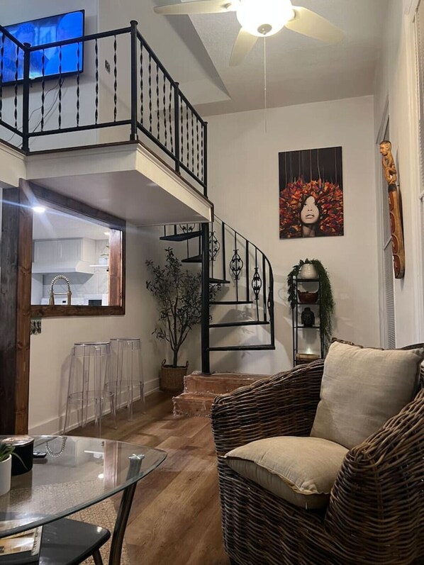 Un'ampia zona giorno con soffitto alto, una scala, un tavolo da pranzo e un divano in vimini.