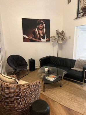 Un soggiorno con un divano nero, un tavolino in vetro, una poltrona nera, una poltrona in vimini e un grande quadro appeso al muro.