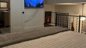 A bedroom with a bed, a ceiling fan, a TV mounted on the wall, and a staircase with a railing.
