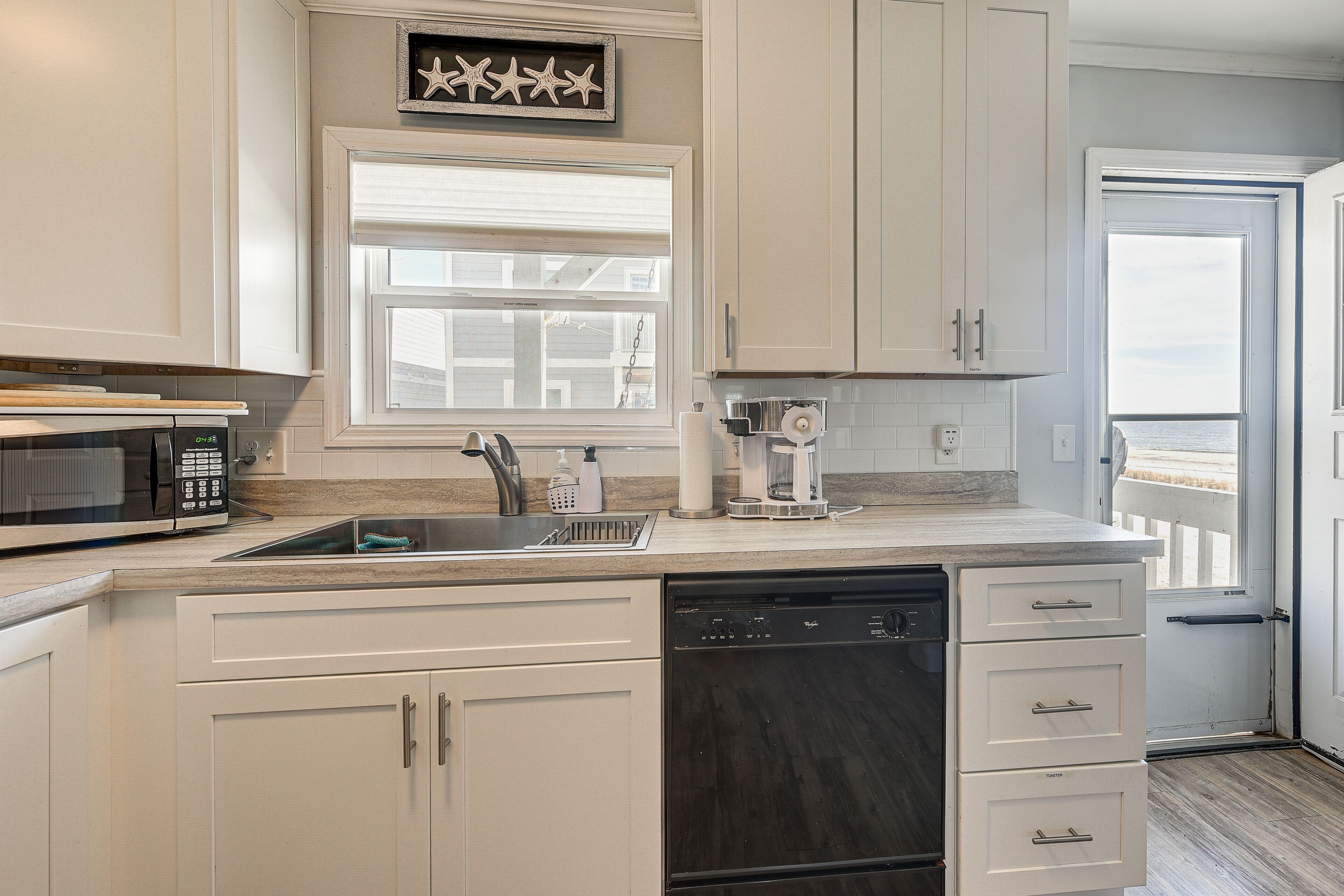 A kitchen with white cabinets, a dishwasher, a microwave, and a coffee maker.