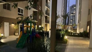 Ein Wohngebäude mit Spielplatz, Kübelpflanzen und einem gut beleuchteten Weg.