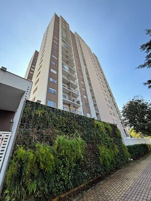 Um edifício residencial alto com várias sacadas, uma parede coberta de vegetação e um passeio pavimentado.