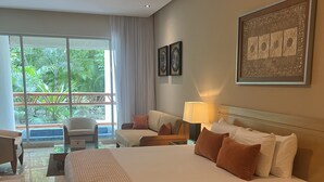 A spacious bedroom with a large bed, a desk, a chair, and a view of greenery through large windows. - Come and spend time in our beautiful resort, Grand Myan, Neuvo Vallarta. (Nuevo Vallarta)
