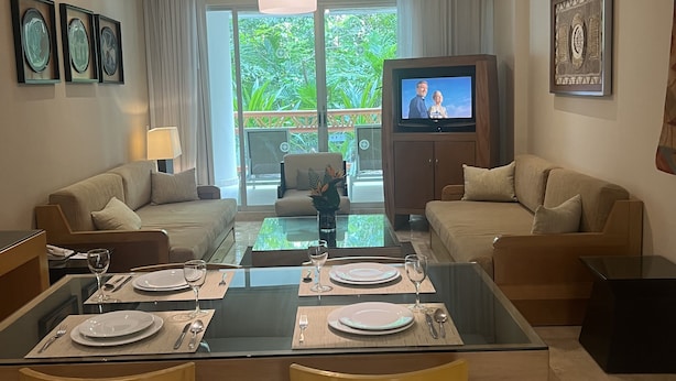 A modern living room with a glass dining table set for two, a sofa, a television, and a ceiling fan. - Come and spend time in our beautiful resort, Grand Myan, Neuvo Vallarta. (Nuevo Vallarta)