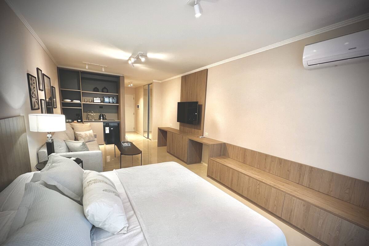 Habitació d'hotel moderna amb un llit gran, una taula de treball, una cadira, un televisor i una nevera bar.