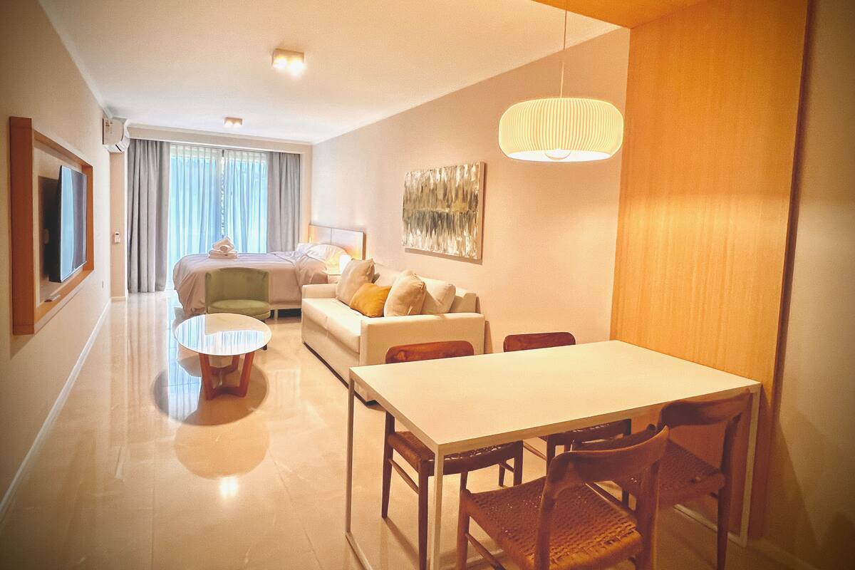Una habitació d'hotel moderna amb zona de menjador, sofà, llit i televisió.