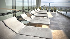 Une terrasse sur le toit, dotée de chaises longues, d’une balustrade en verre et offrant une vue sur la ville.