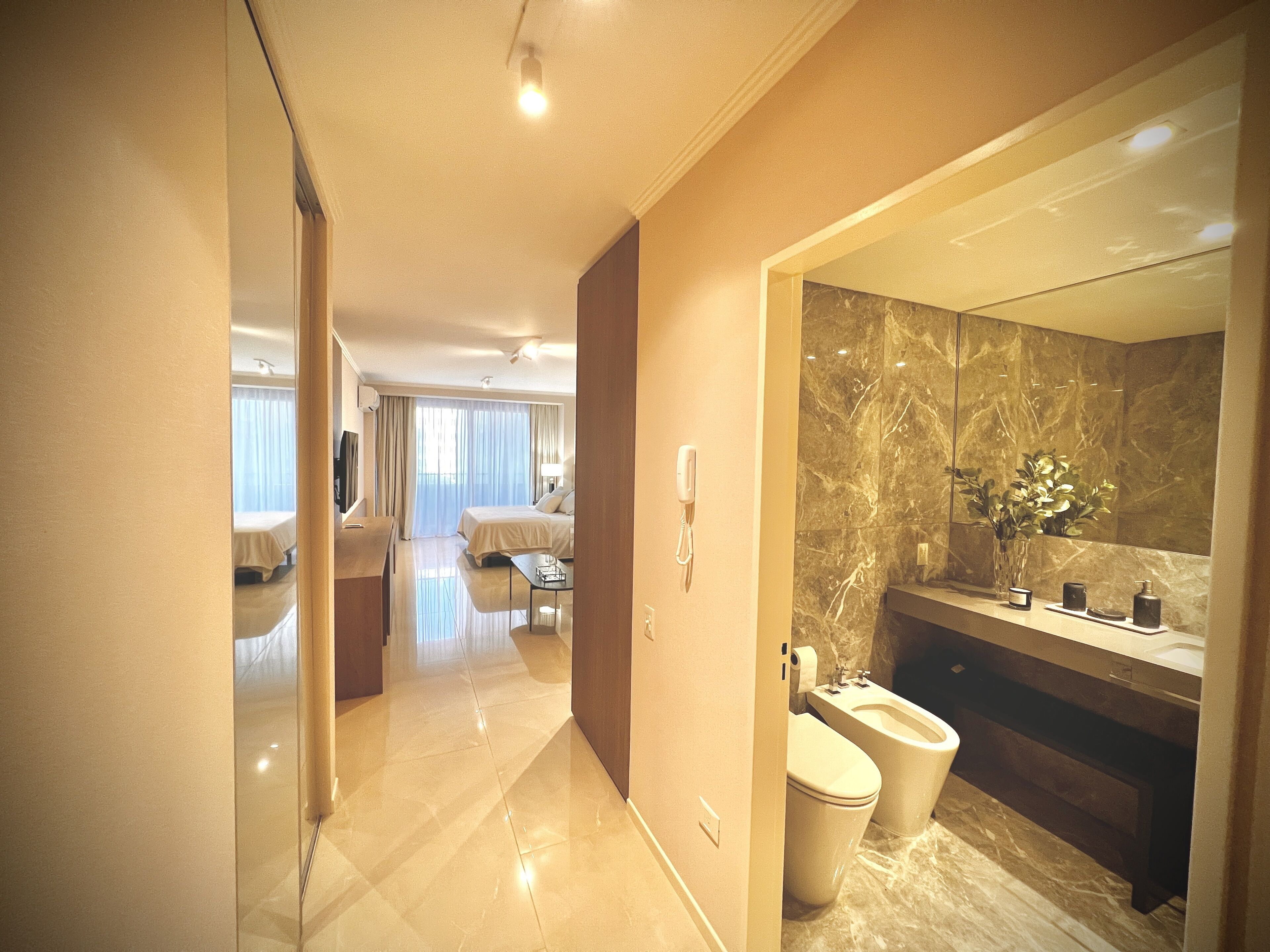 Un moderno baño de hotel con tocador de mármol, un espejo grande y un área de aseo separada.