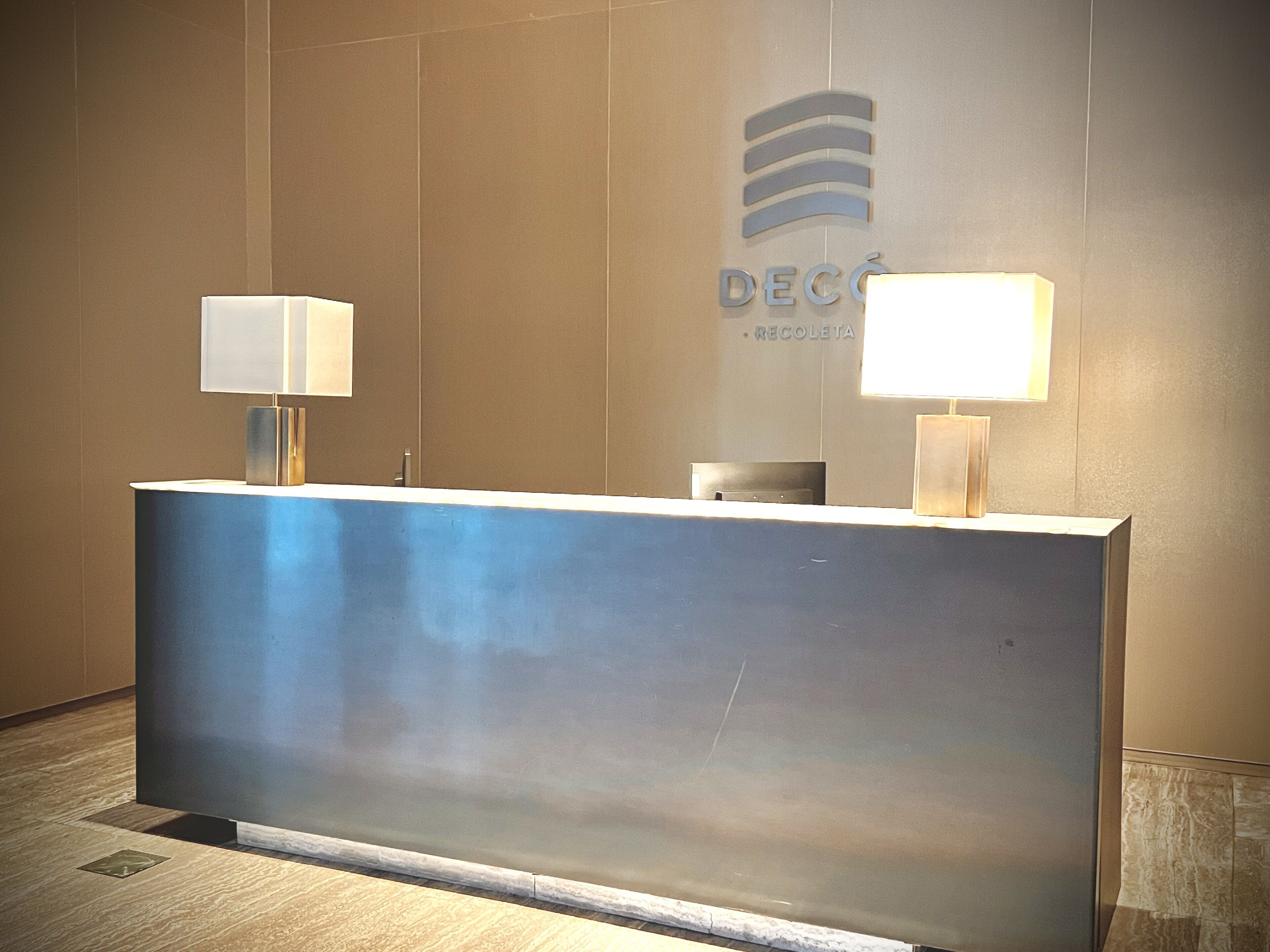 A reception desk with two wall-mounted lamps, a logo, and a trash bin.