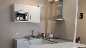 Una cocina compacta con muebles blancos, un microondas integrado, una estufa a gas y un refrigerador pequeño.
