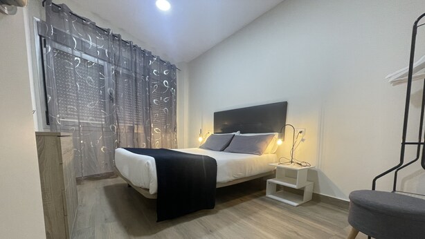 Un dormitorio moderno con cama, mesita de noche, silla y cortina estampada.