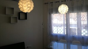 Un comedor con mesa y sillas de vidrio, dos lámparas colgantes y un ventanal con cortinas estampadas.